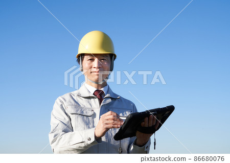一個戴著頭盔的男人在藍天下拿著平板電腦 86680076