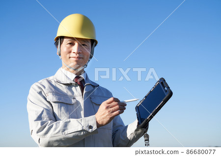 一個戴著頭盔的男人在藍天下拿著平板電腦 86680077