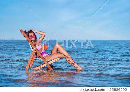 Happy beautiful woman in a pink bathing suit relaxing on the beach while lying at the deck chair Happy beautiful woman in a pink bathing suit relaxing on the beach while lying at the deck chair 86686900