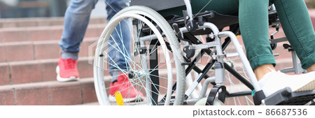 Man lifts wheelchair with a woman on stairs closeup Man lifts wheelchair with a woman on stairs closeup 86687536