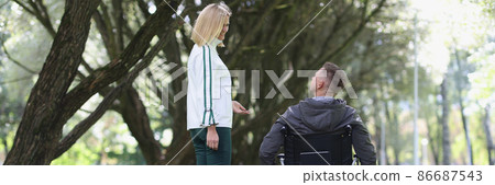 Young smiling woman walks in park with man in wheelchair 86687543