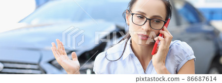Upset young woman talking on phone against background of broken car 86687614