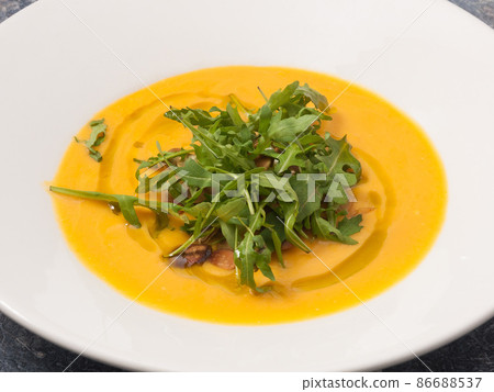 cream of pumpkin soup with arugula on a white plate cream of pumpkin soup with arugula on a white plate 86688537