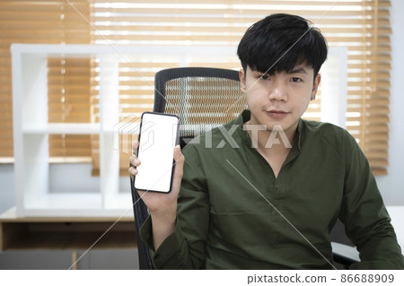 Handsome young asian man holding and showing smart phone with blank screen. 86688909