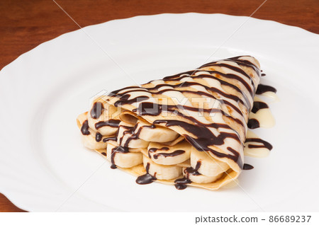 crepe with banana and chocolate on a white plate crepe with banana and chocolate on a white plate 86689237