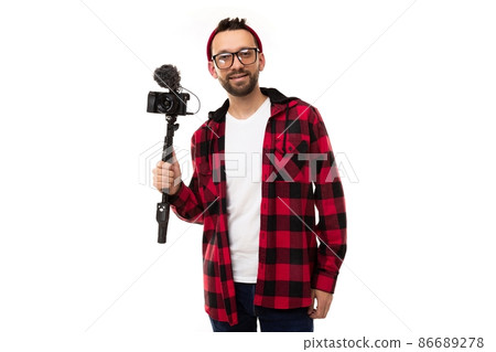 a young blogger on a white background in a plaid shirt and glasses for vision holds a camera with a 86689278