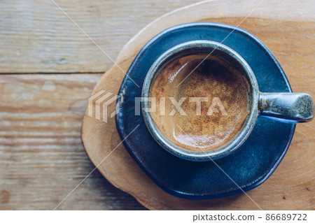 A cup of hot espresso shot on the wooden table. Espresso is a full-flavored It is made by forcing pressurized, hot water through very finely ground coffee beans. 86689722