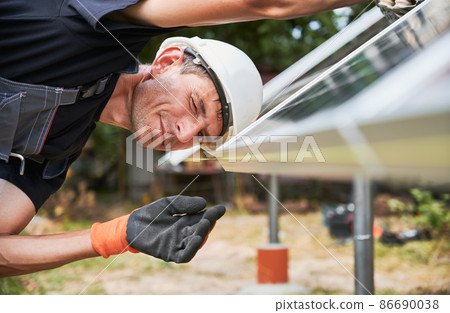 Worker looking on evenness of solar panel during installing. Renewable and ecological energy. Idea of environment safe. Modern technology and innovation. European man wearing workwear and helmet Worker looking on evenness of solar panel during installing. Renewable and ecological energy. Idea of environment safe. Modern technology and innovation. European man wearing workwear and helmet 86690038