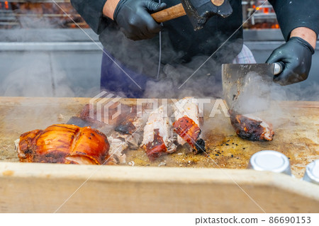 Street grill, fried meat. A man cuts a fried piece of meat into portion. Traditional christmas street food fair in Monaco. Street grill, fried meat. A man cuts a fried piece of meat into portion. Traditional christmas street food fair in Monaco. 86690153