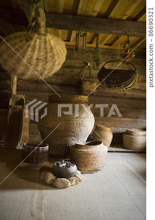An old wooden hut and a barn made of round logs. Interior decoration. Barrels, pots, cast-iron pots, wicker baskets, spinning wheels and spindles, churn. An old wooden hut and a barn made of round logs. Interior decoration. Barrels, pots, cast-iron pots, wicker baskets, spinning wheels and spindles, churn. 86690321