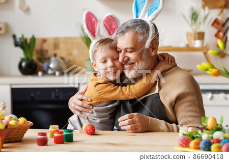 Happy family loving grandfather and cute little boy grandson embracing while painting Easter eggs Happy family loving grandfather and cute little boy grandson embracing while painting Easter eggs 86690418