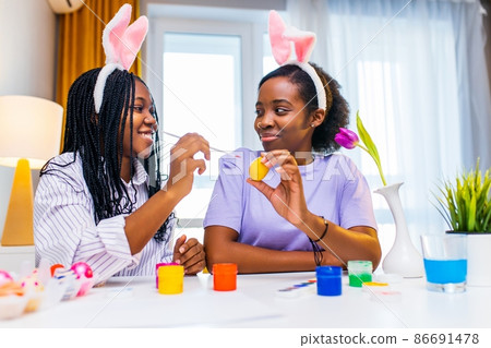 multiracial two women painting eggs with cute pink rabbit costume ears in apartment multiracial two women painting eggs with cute pink rabbit costume ears in apartment 86691478