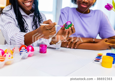 multiracial two women painting eggs with cute pink rabbit costume ears in apartment 86691563