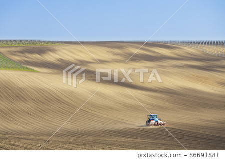Tractor with seed drill in early spring landscape Tractor with seed drill in early spring landscape 86691881