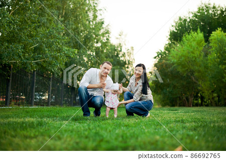 Happy family mother, father, child daughter. Happy young family spending time together outside in green nature. Happy family resting together on the green grass. Happy family having fun outdoors 86692765