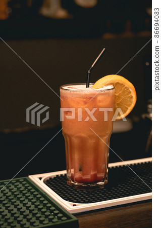 Refreshing iced cocktail tequila sunrise in tall glass with orange slice and straw on bar counter 86694083