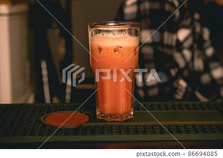 Glass with refreshing alcoholic cocktail with orange juice and ice on bar counter 86694085