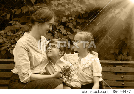 Mother and kids sitting in park on bench 86694487