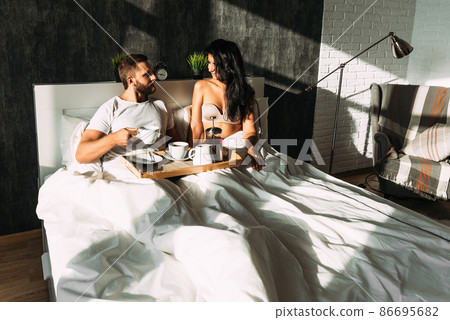 Beautiful couple in bed. Lovers in bed. Happy loving couple having breakfast in bed. Family relationships. Young couple drinking tea. Man and woman having Breakfast in their bedroom 86695682