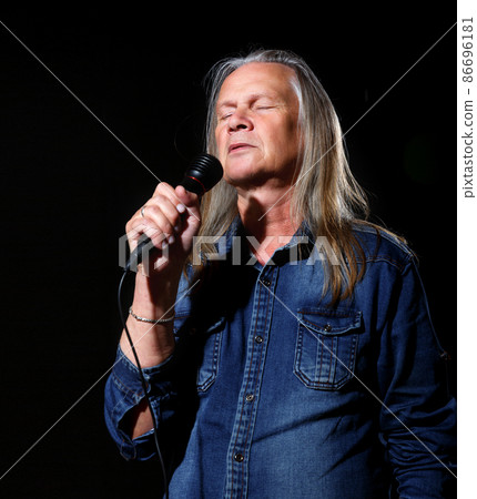 elderly man with long gray hair in blue denim shirt sings into a microphone elderly man with long gray hair in blue denim shirt sings into a microphone 86696181