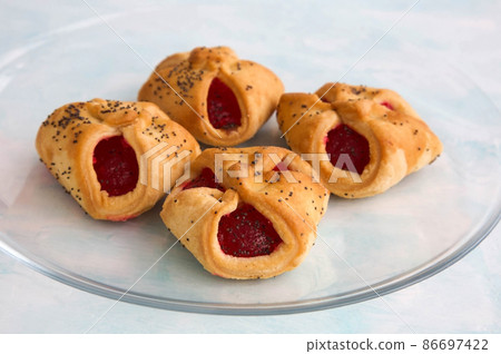 Homemade crunchy butter cookies envelopes with jam and poppy seeds on a transparent glass plate 86697422