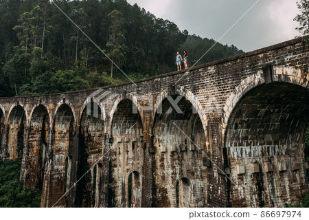 Loving couple on the edge of the bridge. Man and woman traveling around Asia. The couple travels to Sri Lanka. Man and woman in an unusual place. Nine-arch bridge. Travellers in Asia. Hold hands Loving couple on the edge of the bridge. Man and woman traveling around Asia. The couple travels to Sri Lanka. Man and woman in an unusual place. Nine-arch bridge. Travellers in Asia. Hold hands 86697974