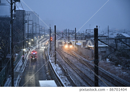 雪黃昏鐵路風景接近的火車車頭燈在鐵軌旁邊運行的卡車屋頂 雪黃昏鐵路風景接近的火車車頭燈在鐵軌旁邊運行的卡車屋頂 86701404