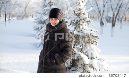 A brunette woman in winter clothes walks through the winter forest A brunette woman in winter clothes walks through the winter forest 86702447