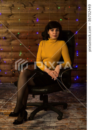 A brunette woman in a bright yellow turtleneck behind a huge leather chair A brunette woman in a bright yellow turtleneck behind a huge leather chair 86702449