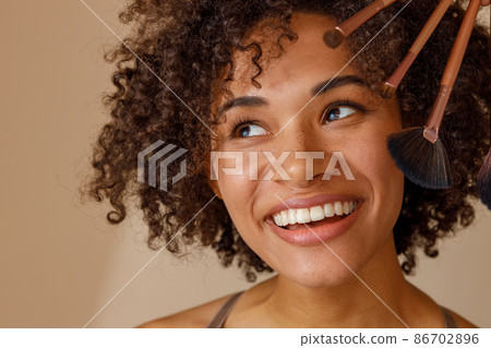Charming woman demonstrating makeup tools against beige wall Charming woman demonstrating makeup tools against beige wall 86702896