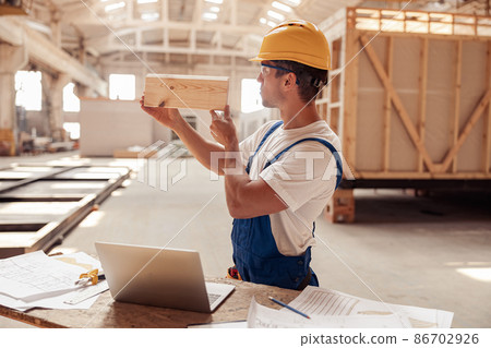 Male builder checking wooden plank at construction site 86702926