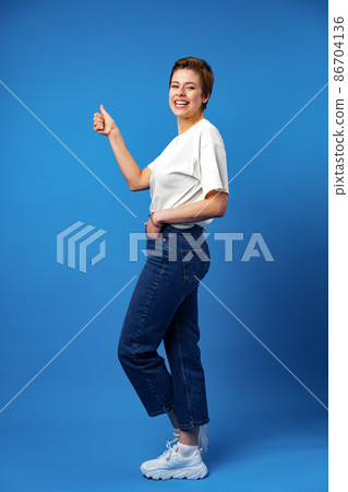 Young happy cheerful woman with short hair showing thumb up on blue background Young happy cheerful woman with short hair showing thumb up on blue background 86704136