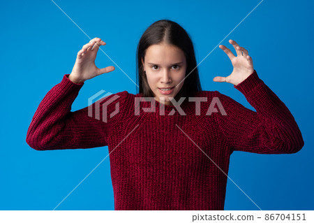 Young annoyed angry woman holding hands in furious gesture on blue background Young annoyed angry woman holding hands in furious gesture on blue background 86704151