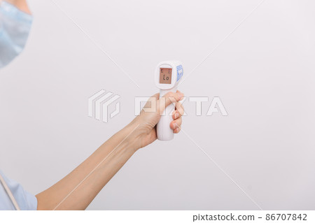 Temperature measurement gun in doctor hands. Close-up shot of doctor wearing protective surgical mask ready to use infrared isometric thermometer gun to check body temperature for virus symptoms. Temperature measurement gun in doctor hands. Close-up shot of doctor wearing protective surgical mask ready to use infrared isometric thermometer gun to check body temperature for virus symptoms. 86707842