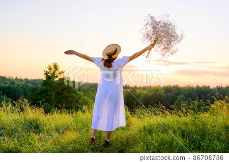 Back view of romantic woman in a white dress with a straw hat enjoying sunset Back view of romantic woman in a white dress with a straw hat enjoying sunset 86708786