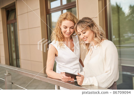 Pretty young women texting by tablet. Two happy female persons outdoors 86709094