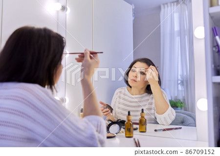 Beautiful middle aged woman doing makeup in front of a mirror. 86709152