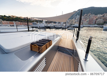 The front deck of huge yacht in port of Monaco at sunset, the place for landing of helicopter, a lot of motorboats are on background, the chrome plated handrail, megayacht is moored in marina, dusk 86709717