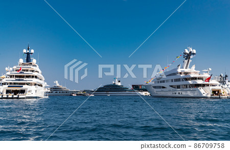 A lot of huge yachts are in port of Monaco at sunny day, Monte Carlo, mountain is on background, glossy board of the motor boat, megayachts are moored in marina, sun reflection on glossy board A lot of huge yachts are in port of Monaco at sunny day, Monte Carlo, mountain is on background, glossy board of the motor boat, megayachts are moored in marina, sun reflection on glossy board 86709758