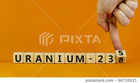 Uranium enrichment symbol. Hand turns cube and changes words 'uranium-238' to 'uranium-235'. Beautiful orange background, copy space. Business, nuclear technology and uranium enrichment concept. 86710915
