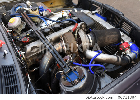 Sports car engine with turbine. An open race car hood on a pit stop while racing on a race track.  86711394