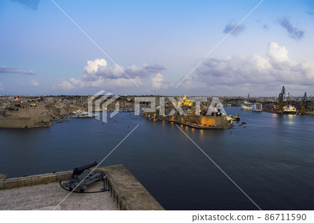 Malta panorama of fortified Three Cities with moored ships and clouds above. Malta panorama of fortified Three Cities with moored ships and clouds above. 86711590
