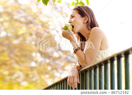Fresh and fruity. Shot of an attractive young woman in the park on an autumn day. 86712192