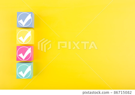 Four white checkmarks in a row on colorful toy cubes against bright yellow background with copy space 86715082