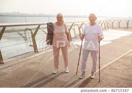 Sportive senior woman and man stand on footbridge at sunset light Sportive senior woman and man stand on footbridge at sunset light 86715387
