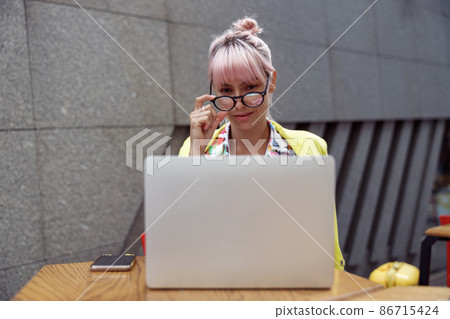 Female straightening glasses while looking at laptop screen outdoors Female straightening glasses while looking at laptop screen outdoors 86715424