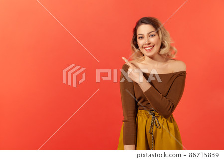 Portrait of cheerful woman with blonde hair pointing finger aside, showing copy space for commercial text, blank wall with idea presentation. Indoor studio shot isolated on red background Portrait of cheerful woman with blonde hair pointing finger aside, showing copy space for commercial text, blank wall with idea presentation. Indoor studio shot isolated on red background 86715839