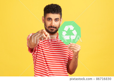 Serious bearded man holding green recycling signboard pointing finger at you looking at camera, calling for garbage sorting and environment protection. Indoor studio shot isolated on yellow background 86716830