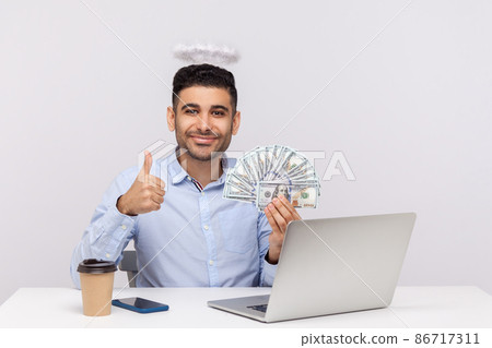 Excellent online earnings. Angelic rich businessman with nimbus on head holding dollars and showing thumbs up, like gesture, sitting at laptop workplace. studio shot isolated on white background Excellent online earnings. Angelic rich businessman with nimbus on head holding dollars and showing thumbs up, like gesture, sitting at laptop workplace. studio shot isolated on white background 86717311