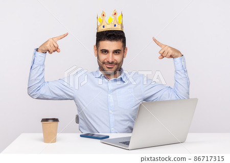 Look, I'm king. Proud authoritative businessman pointing at crown on head while sitting in office workplace, feeling self-confident and ambitious to control company. indoor studio shot isolated Look, I'm king. Proud authoritative businessman pointing at crown on head while sitting in office workplace, feeling self-confident and ambitious to control company. indoor studio shot isolated 86717315
